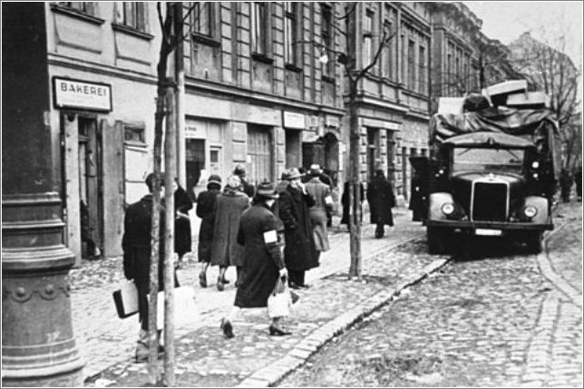 Residents of the Krakow ghetto walk past a German truck loaded with furniture confiscated from Jews. Krakow, Poland, ca. 1941.
